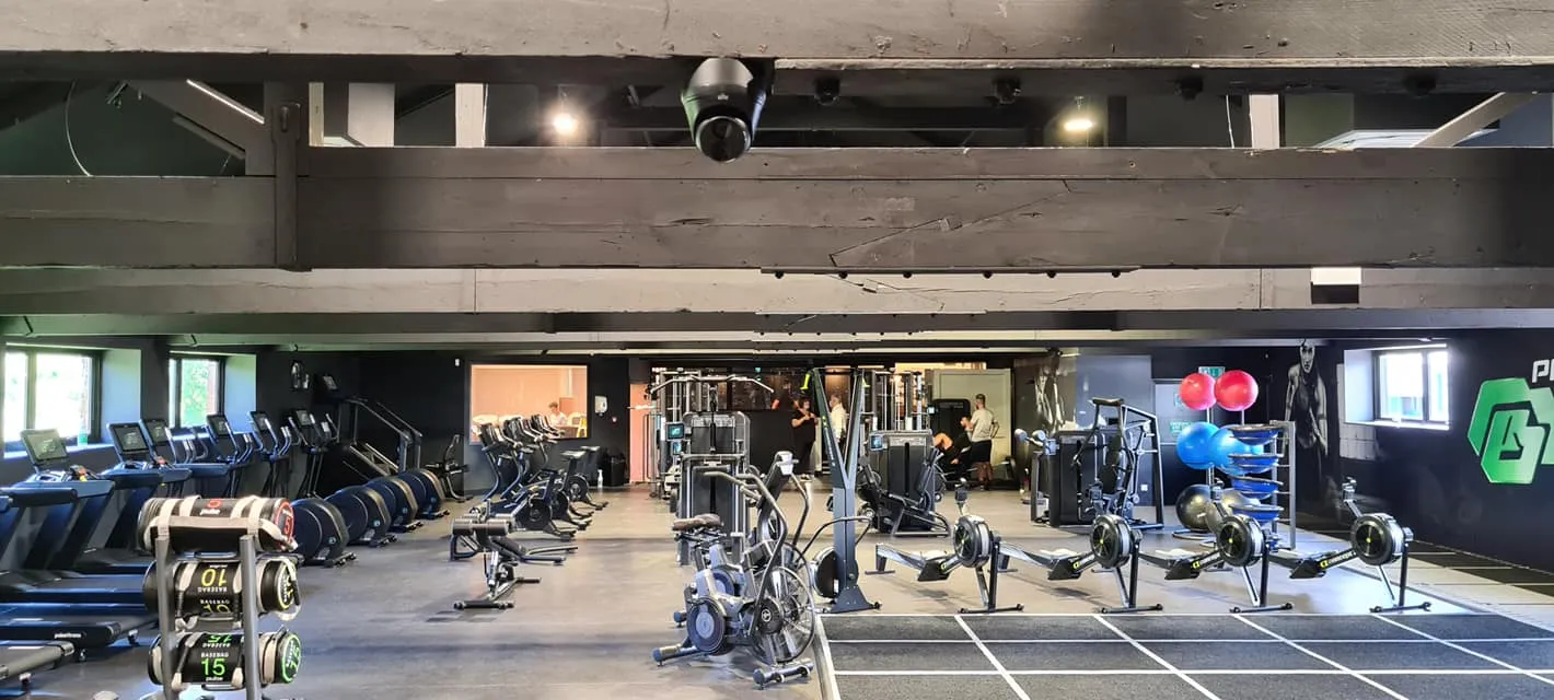Modern gym interior, featuring workout equipment, cardio machines, free weights, and fitness balls. Natural light from windows enhances the space.